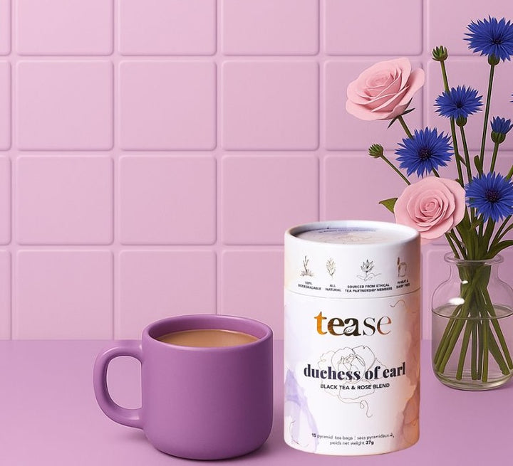 Tease Wellness Duchess of Earl tea blend in white cylindrical tin with purple mug of brewed tea and pink and blue flowers.