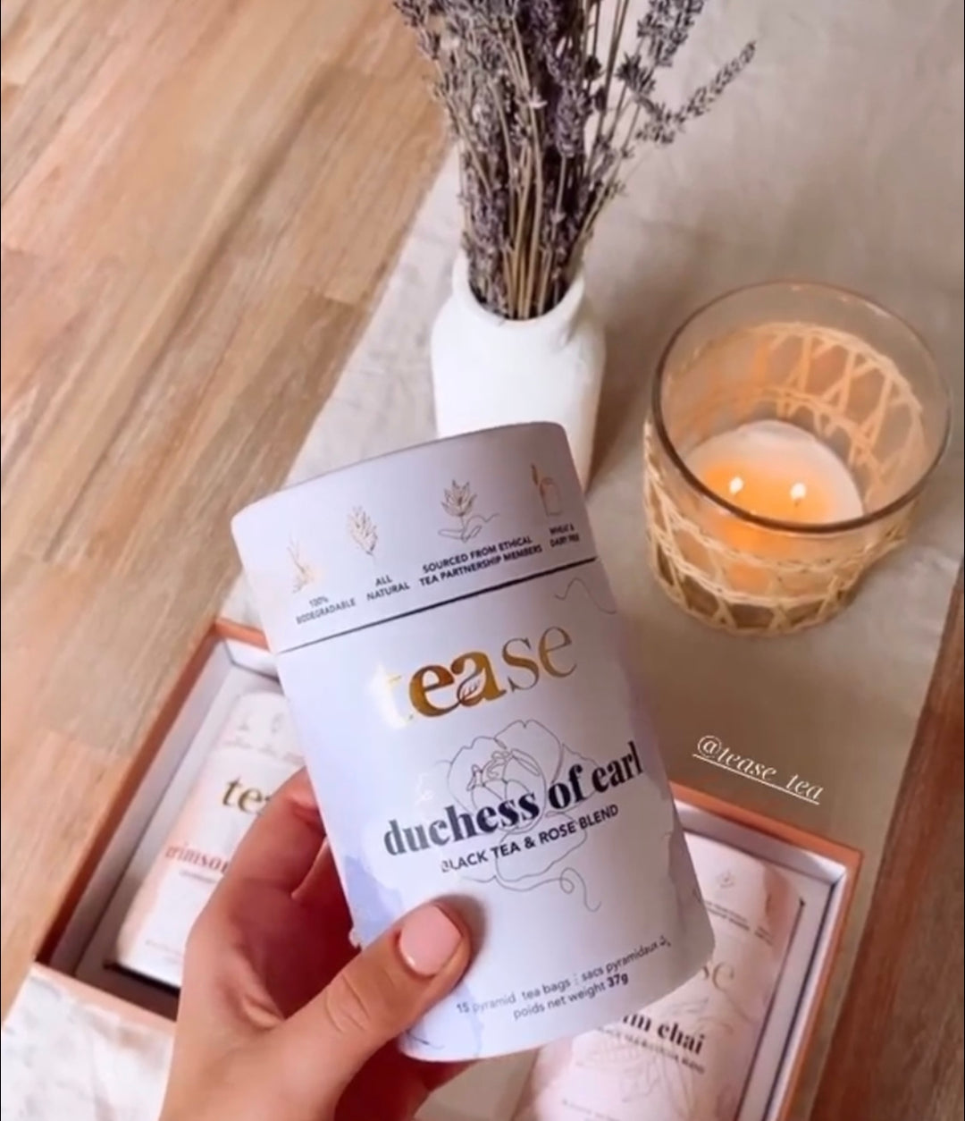 Tease Wellness Duchess of Earl black tea blend tube with floral design held over wooden tray and lit candle.