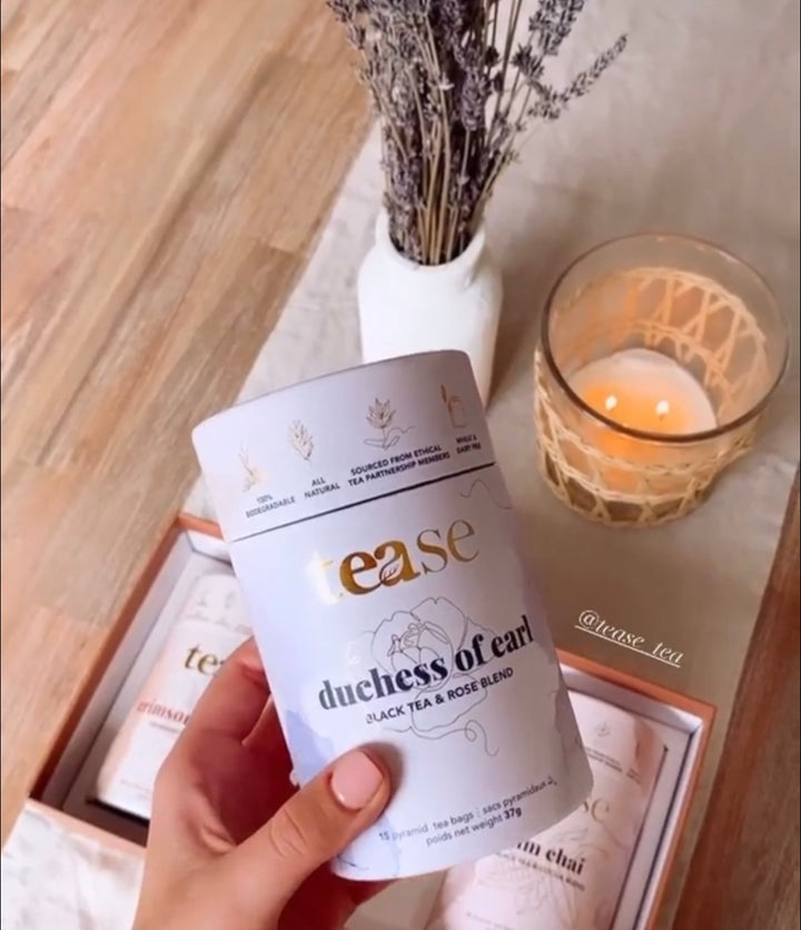 Tease Wellness Duchess of Earl black tea blend tube with floral design held over wooden tray and lit candle.