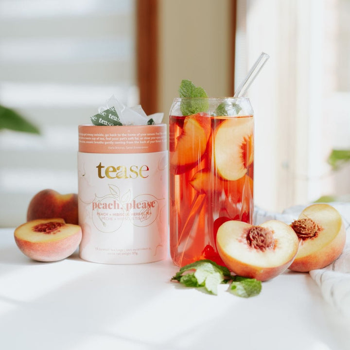 Tease Wellness Peach, Please caffeine-free tea blend in white tube with peach illustrations beside glass of iced peach tea.