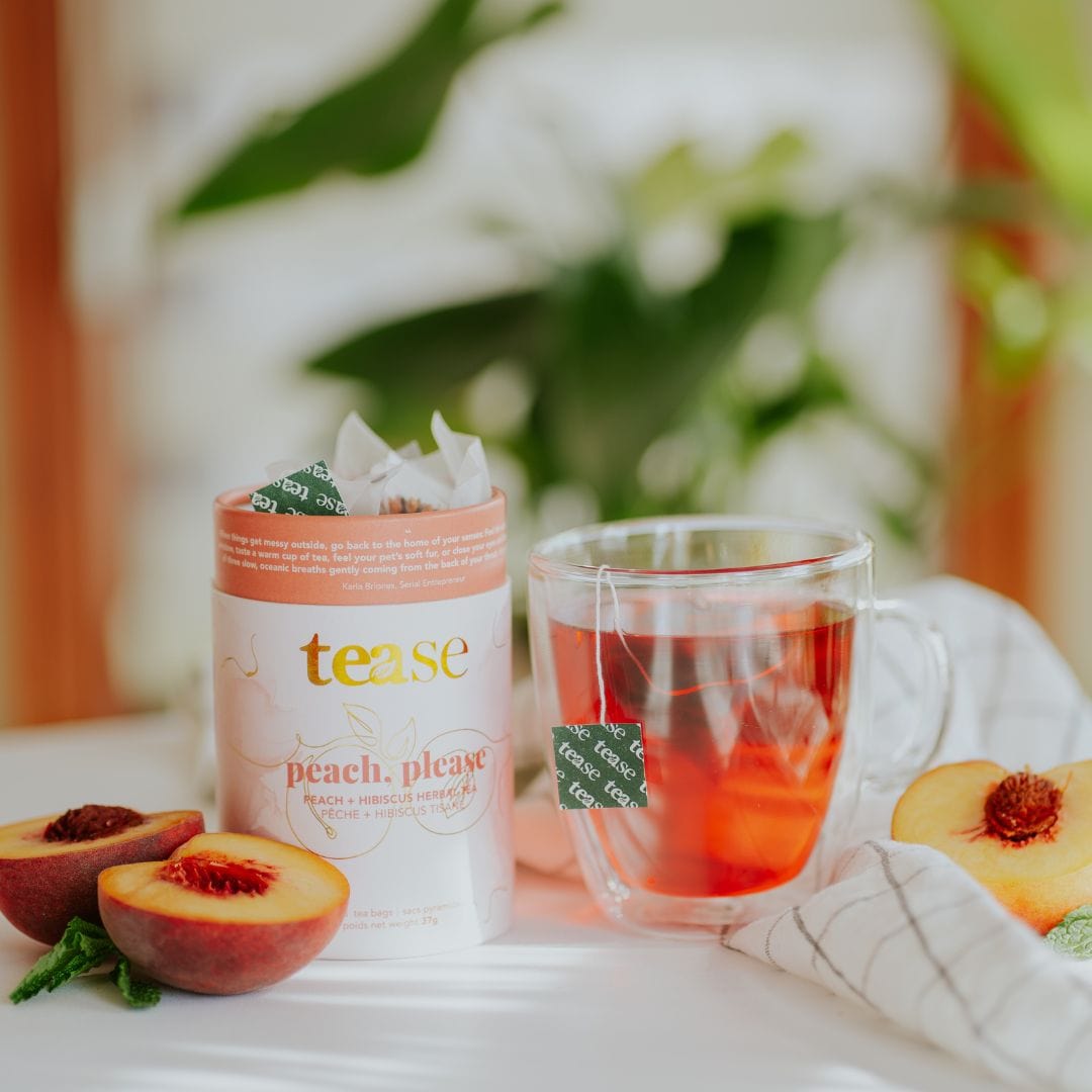 Tease Wellness Peach, Please tea blend in white and peach tube with fresh peaches and clear mug of brewed tea.