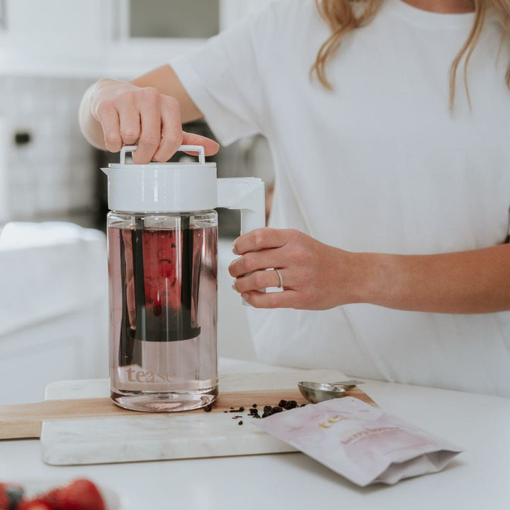 Tease Wellness Cold Brew Iced Tea & Coffee Maker Kit with clear pitcher, white lid, and red hibiscus tea steeping inside.