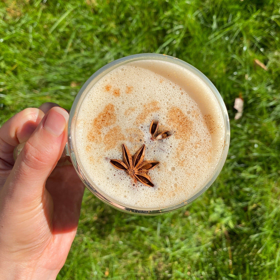 Tease Wellness Aim Chai tea blend topped with star anise and cinnamon in clear glass against grass background.