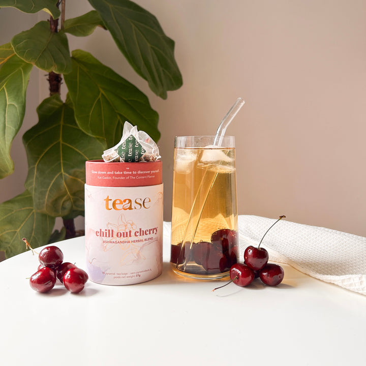 Tease Wellness Chill Out Cherry tea blend in a pink tube with cherries, served in a glass with ice and straw.