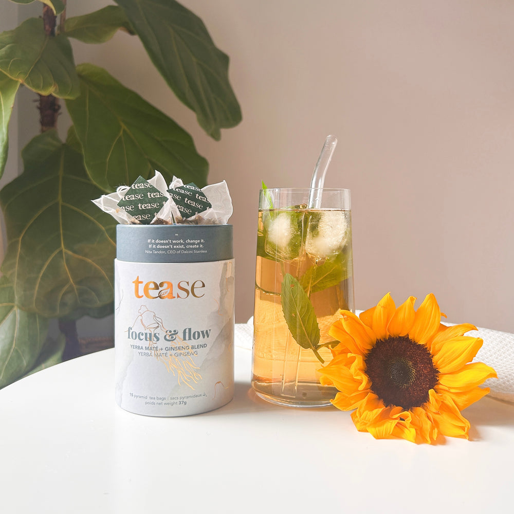 Tease Wellness Focus & Flow tea blend in white cylindrical tube with green tea bag and glass of iced tea garnished with mint .