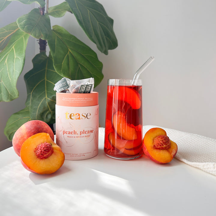 Tease Wellness Peach, Please tea blend in peach-colored tube with loose leaf tea, fresh peaches, and glass of iced peach tea .