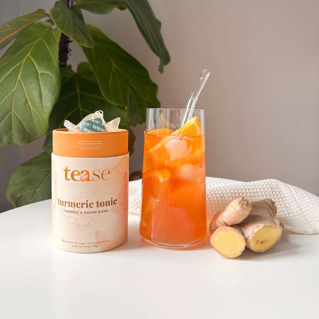 Tease Wellness Turmeric Tonic tea tube with glass of iced turmeric tea and fresh ginger on white table.