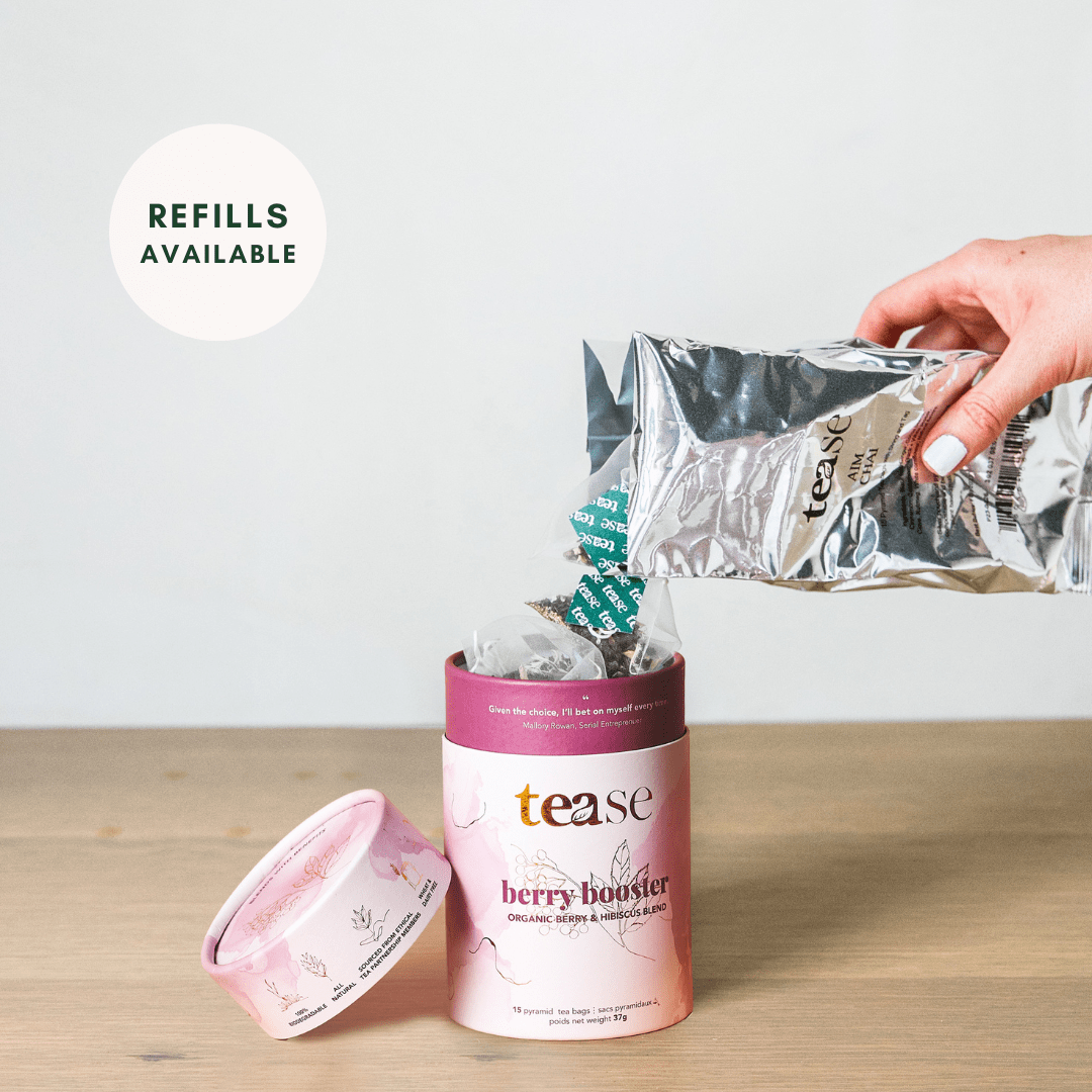 Tease Wellness Berry Booster organic tea blend in pink cylindrical tube with foil refill pouch and hand pouring tea leaves.