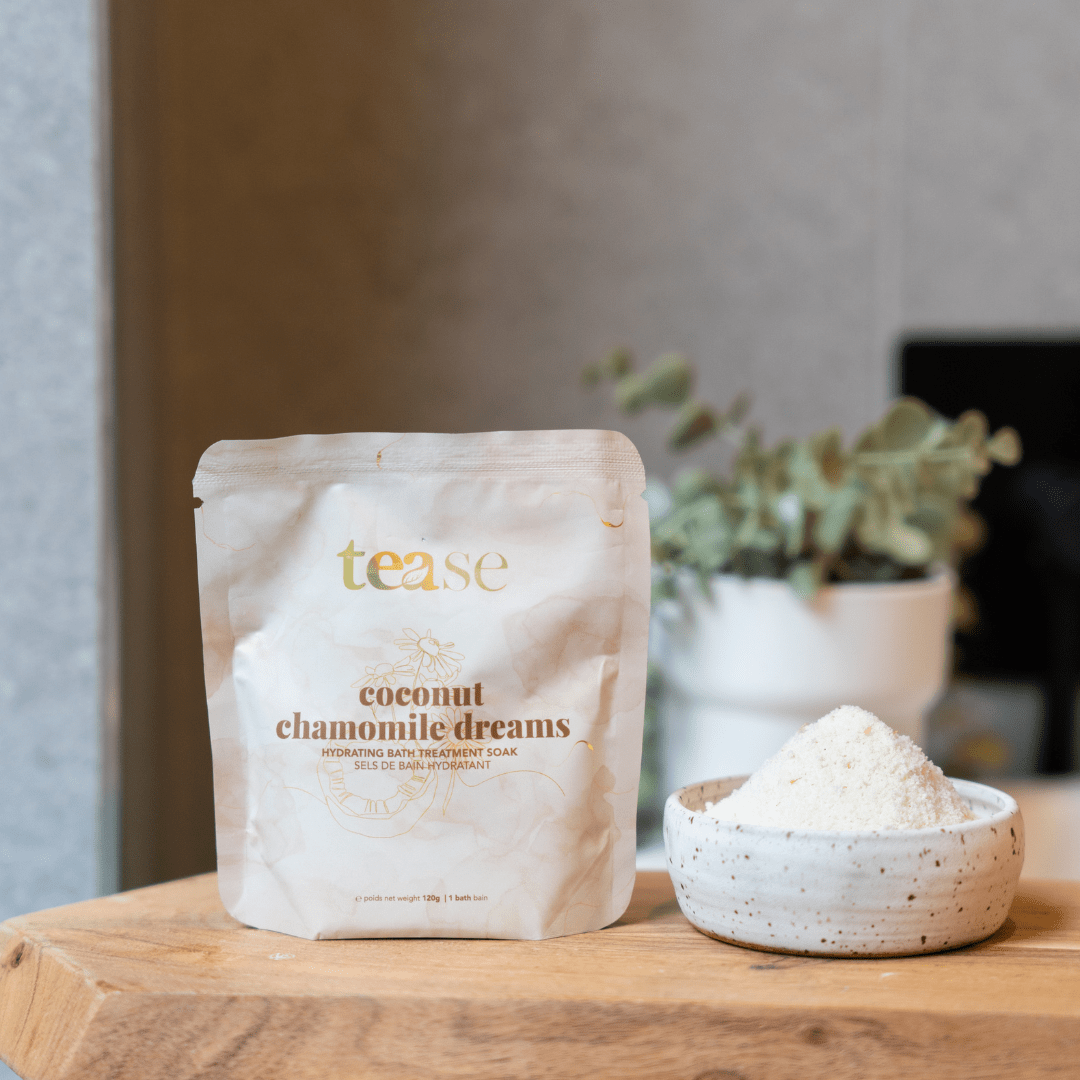 Tease Wellness Coconut Chamomile Dreams Bath Soak in beige resealable pouch with white ceramic bowl of powder on wooden.
