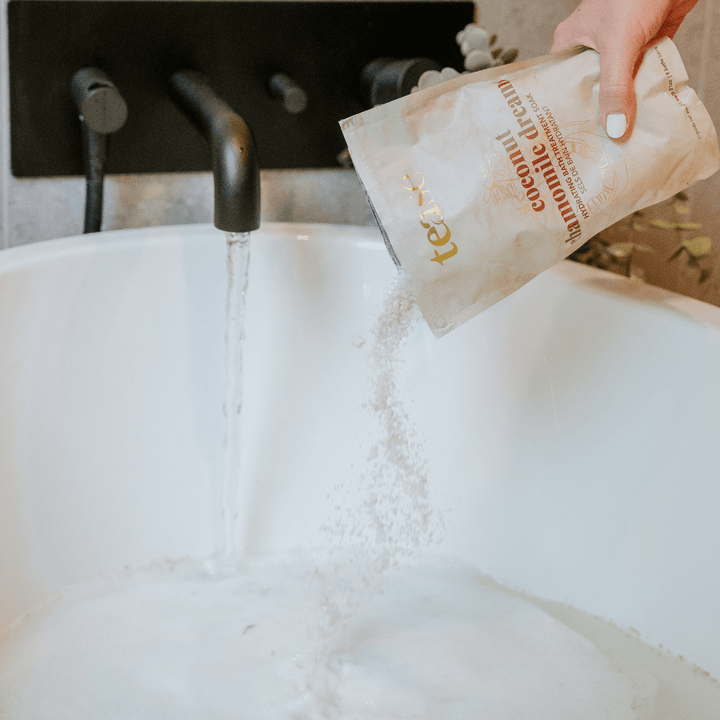 Tease Wellness Coconut Chamomile Dreams Bath Soak pouch pouring white bath salts into white tub under running water.