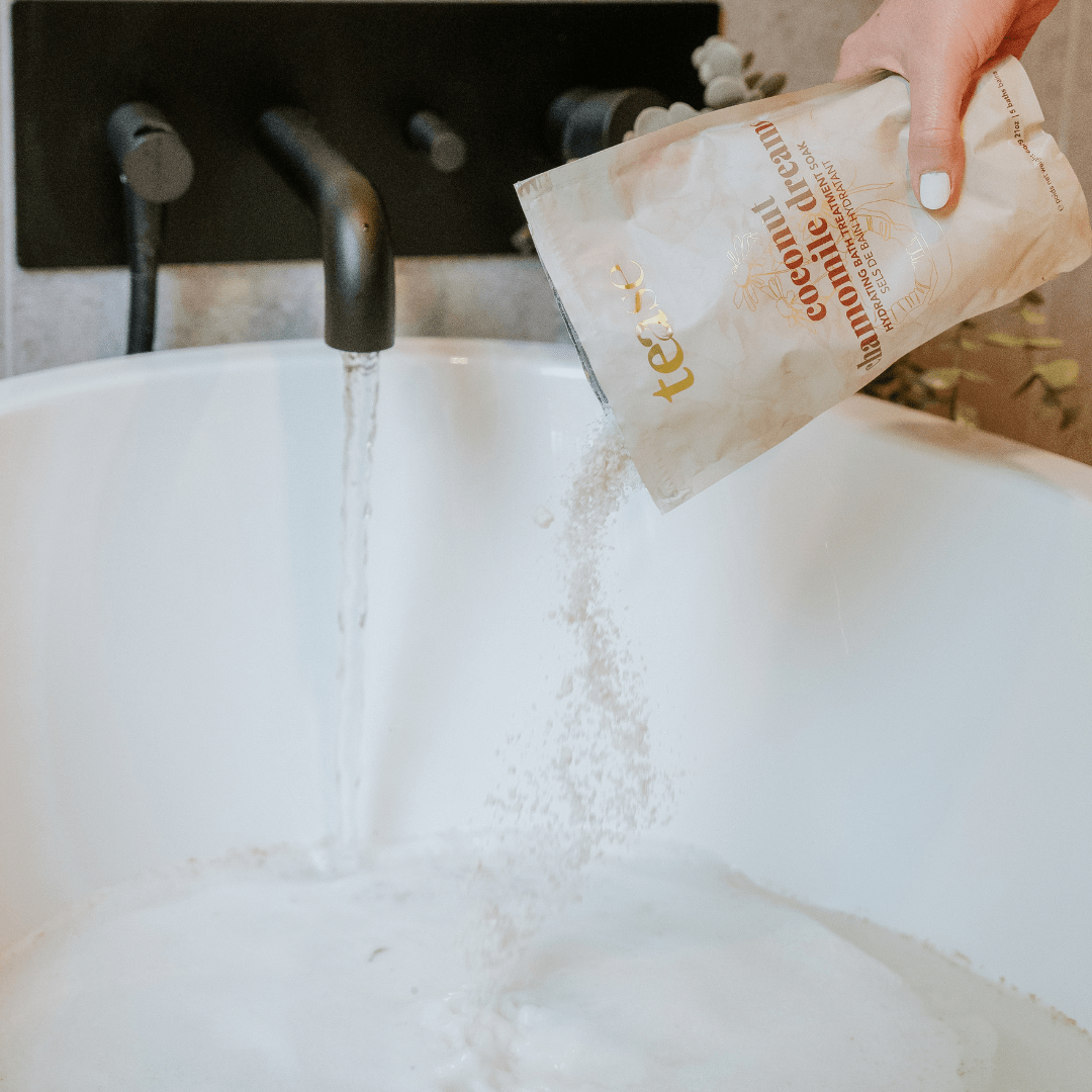 Tease Wellness Coconut Chamomile Dreams Bath Soak pouch pouring white bath salts into white tub under running water.