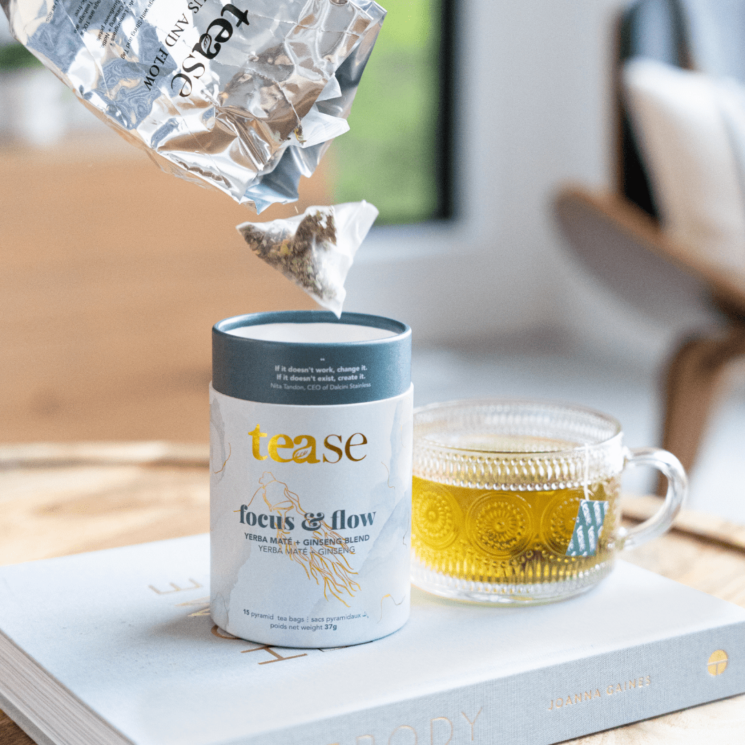 Tease Wellness Focus & Flow tea blend in white cylindrical tube with gray lid beside clear glass cup of brewed golden tea.