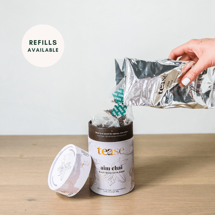 Tease Wellness Aim Chai tea blend in white tube packaging with cinnamon and spices, refill pouch being poured in.