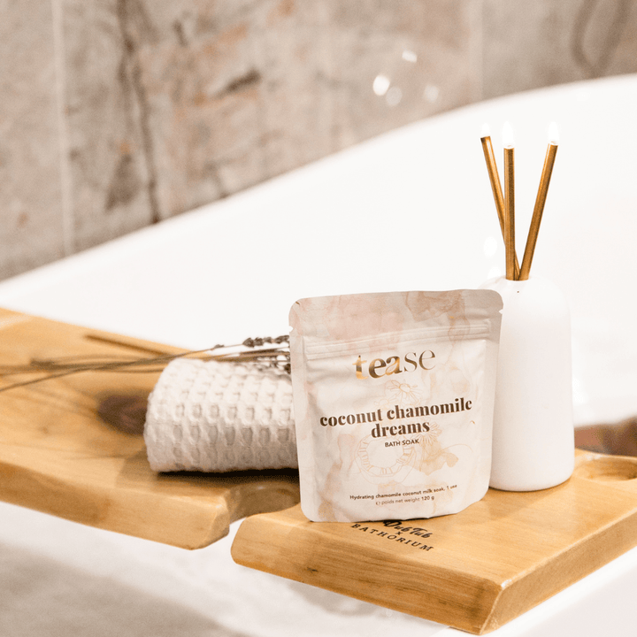 Tease Wellness Coconut Chamomile Dreams bath soak in beige resealable pouch on wooden tray with spa towel and diffuser sticks.