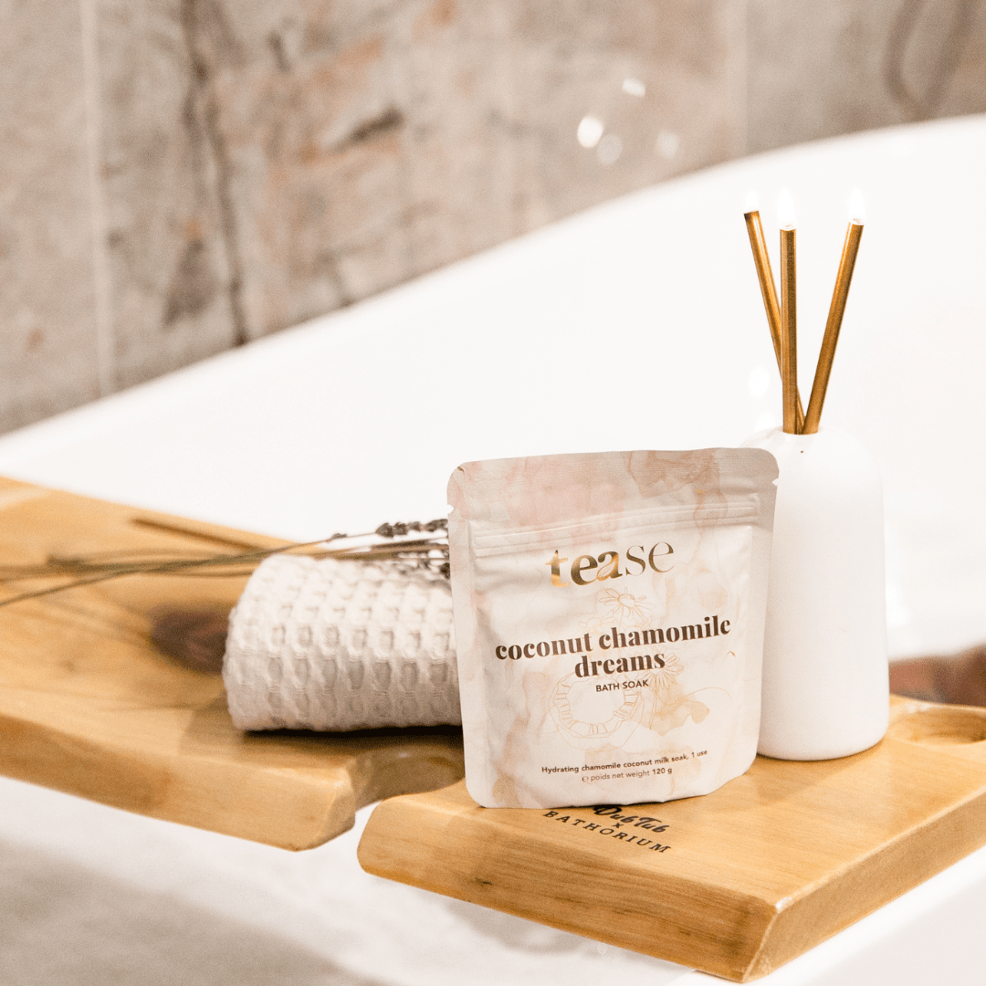 Tease Wellness Coconut Chamomile Dreams bath soak in beige resealable pouch on wooden tray with spa towel and diffuser sticks.