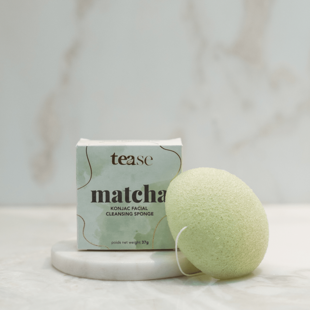 Tease Wellness Matcha Konjac Facial Sponge with green sponge and pastel green packaging on marble surface.