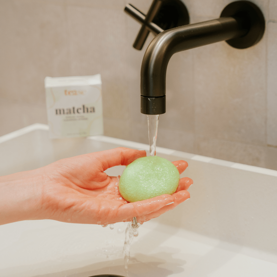 Tease Wellness Matcha Konjac Facial Sponge in hand under running faucet water, light green sponge with smooth texture.
