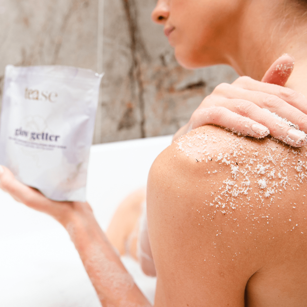 Tease Wellness Glow Getter Earl Grey Body Scrub pouch held by person applying coarse scrub with visible tea blend texture on .